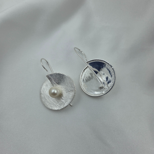 Silver disc with a pearl at the centre on a light gray background