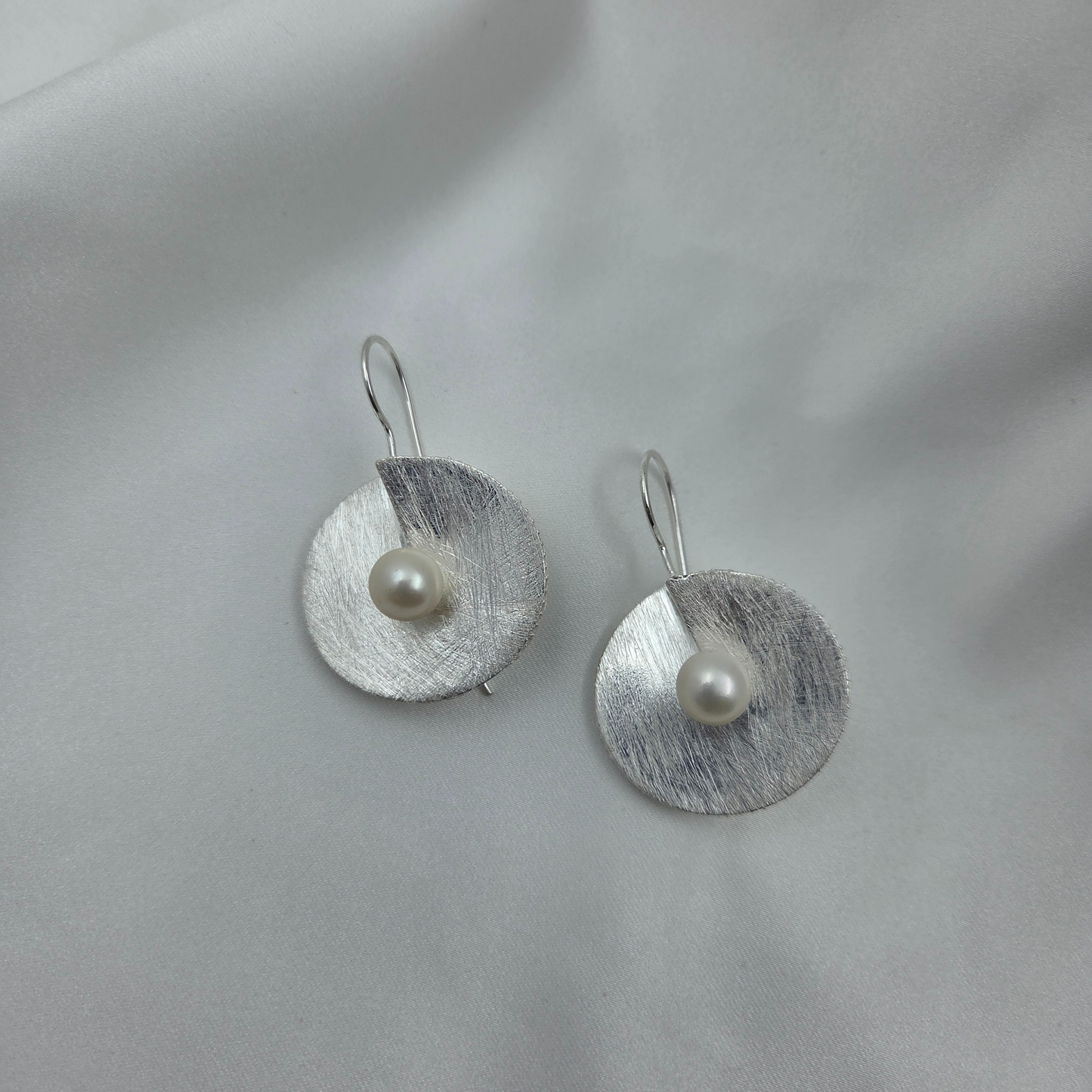 Silver earrings with pearls on a light gray background