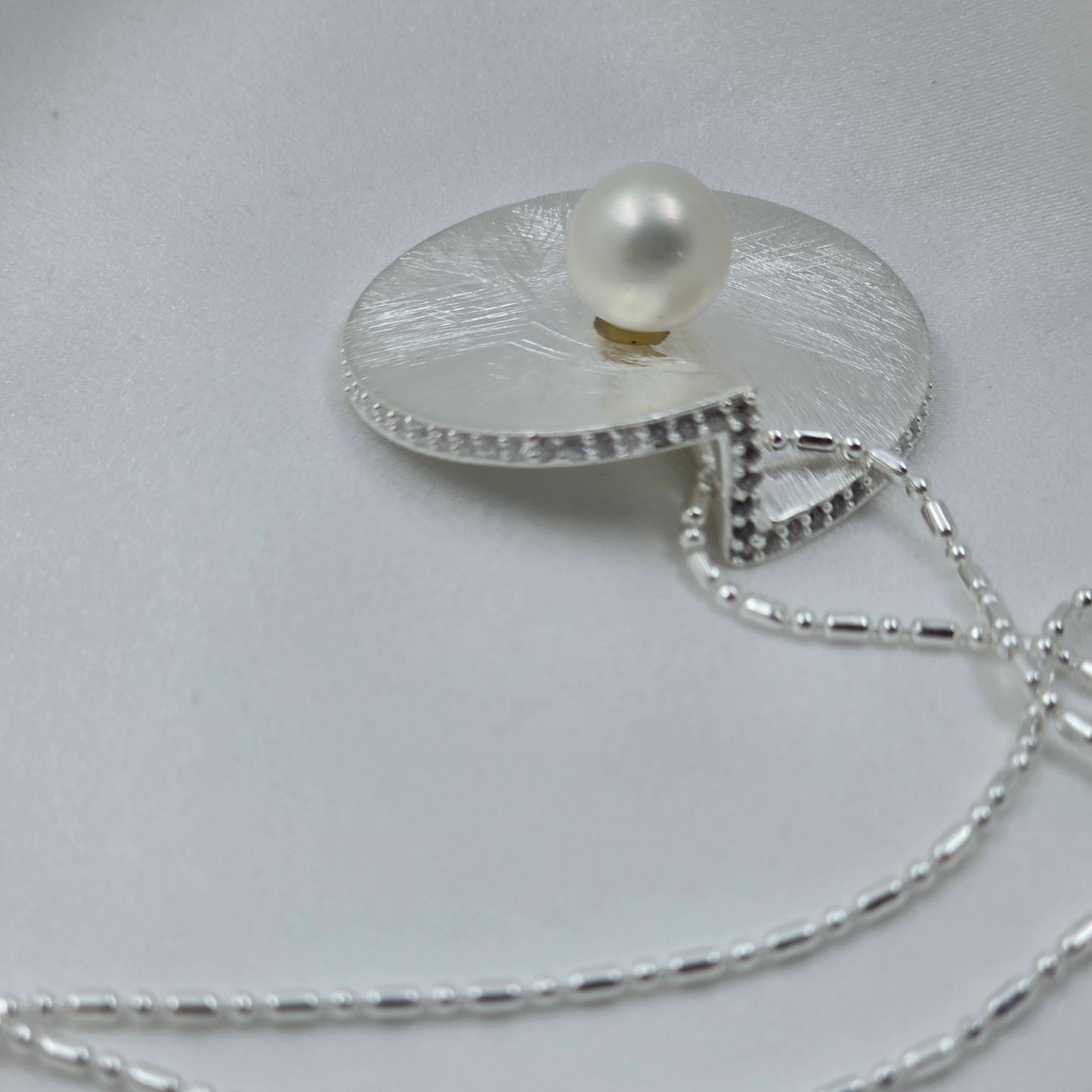 Silver necklace with a pearl pendant on a light gray background