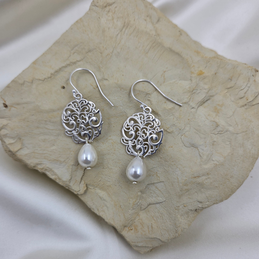 Silver earrings with pearl drops on a stone surface