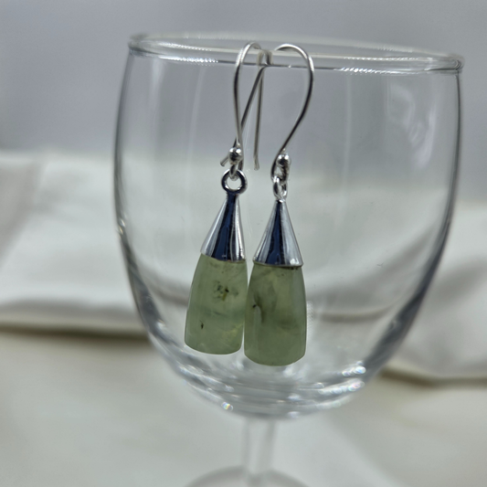 Green stone silver earrings displayed in a clear glass.