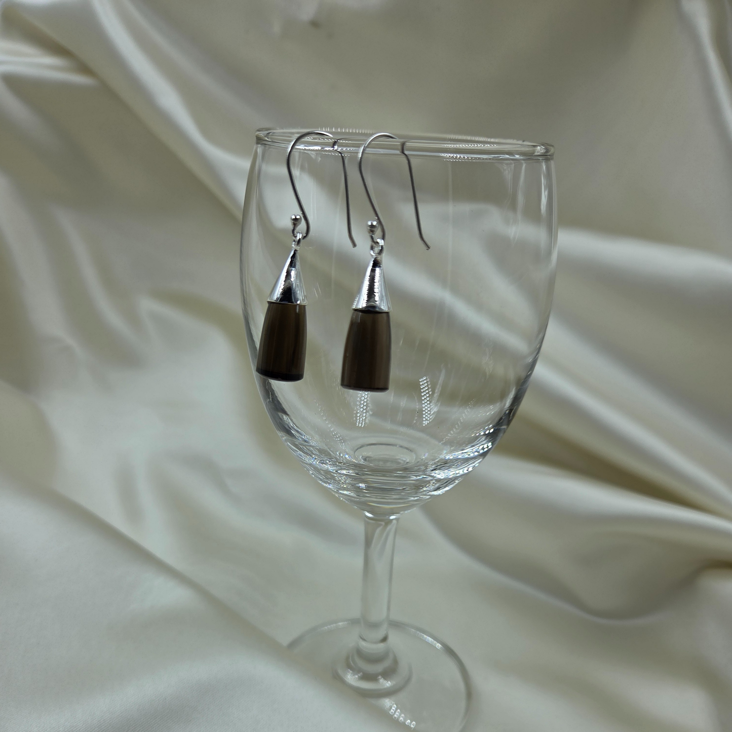 Quartz smokey silver earrings displayed on a glass