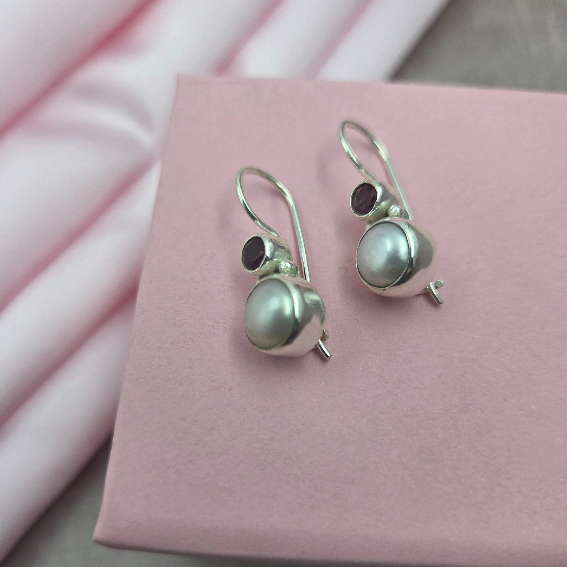 Pair of silver earrings with pearls and garnet stones on a brown stone