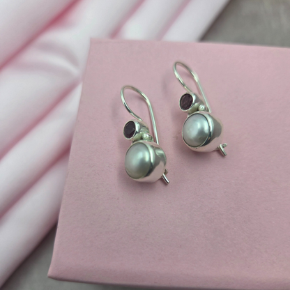 Pair of silver earrings with pearls and garnet stones on a brown stone