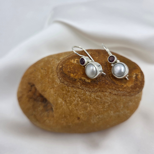 Pair of silver earrings with pearls and garnet stones on a brown stone