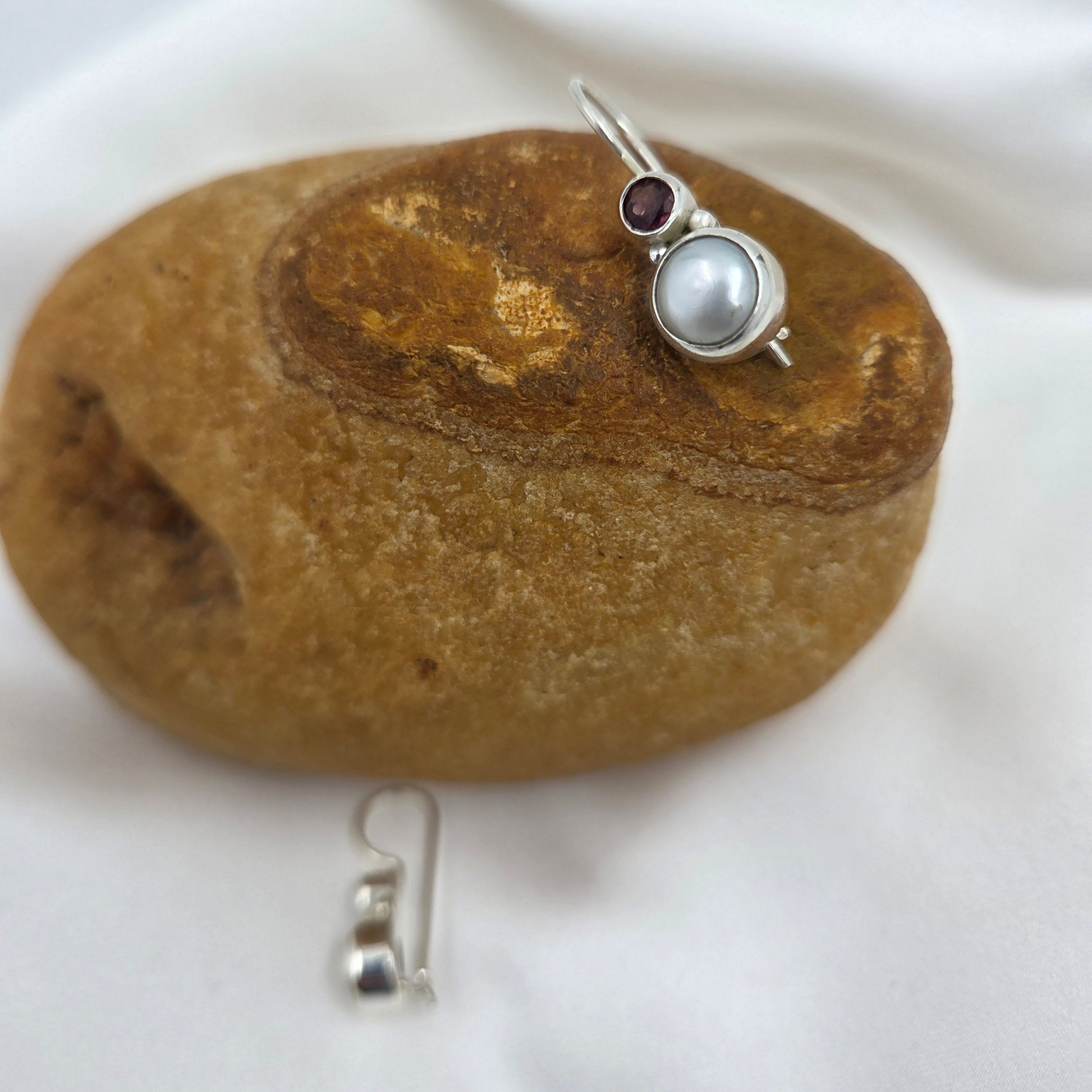 Pair of silver earrings with pearls and garnet stones on a brown stone