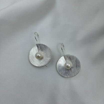 Silver earrings with pearls on a light gray background