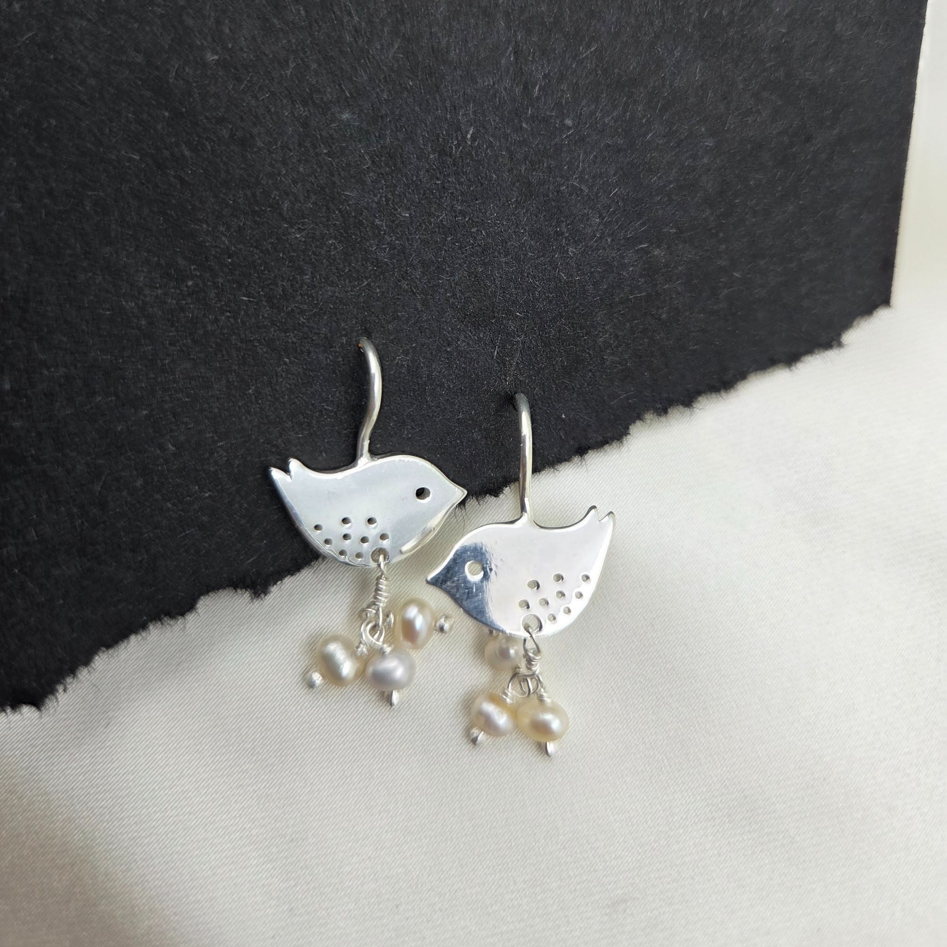 Silver bird-shaped earrings with pearl drops on a black and white background