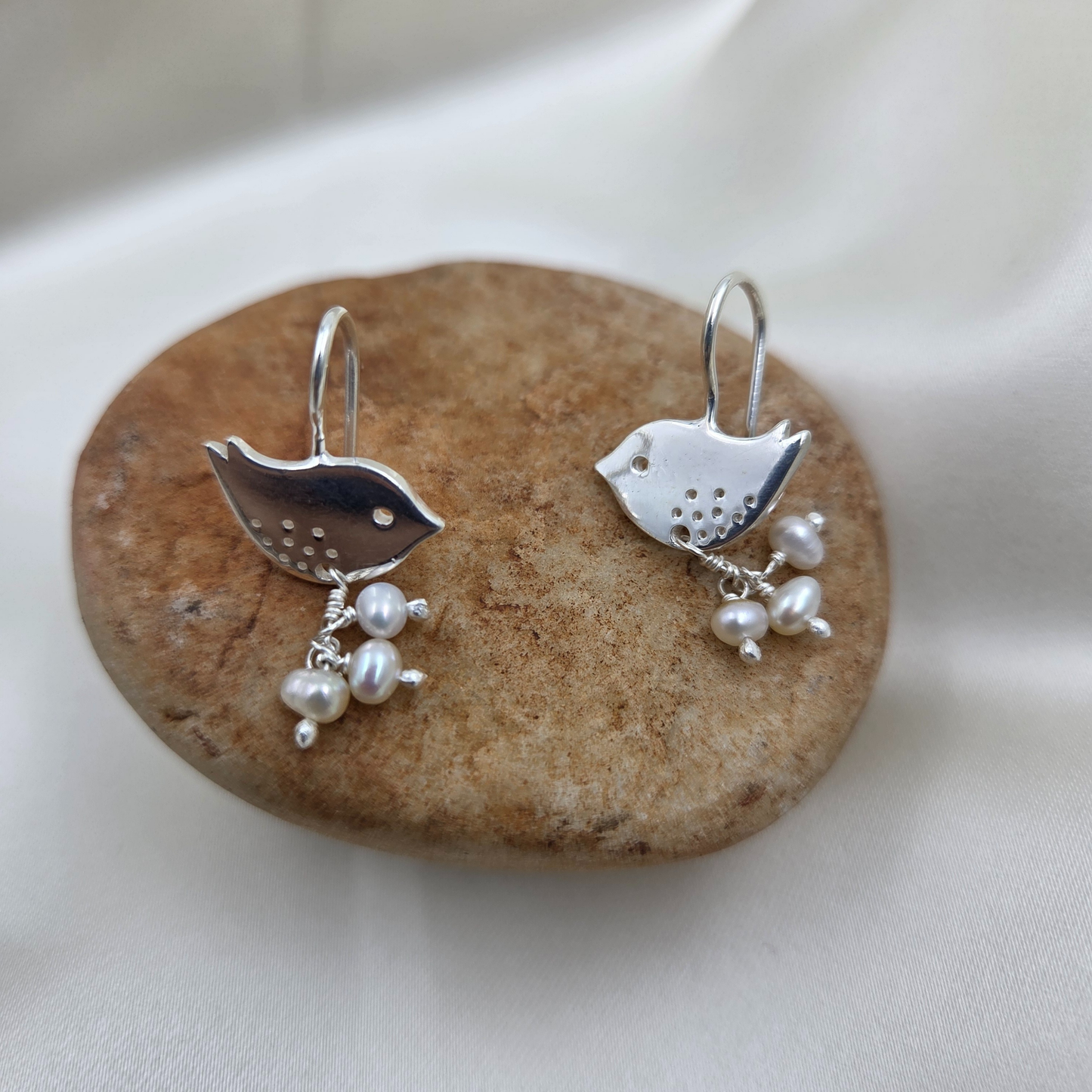 Silver bird-shaped earrings with pearl drops on a stone surface