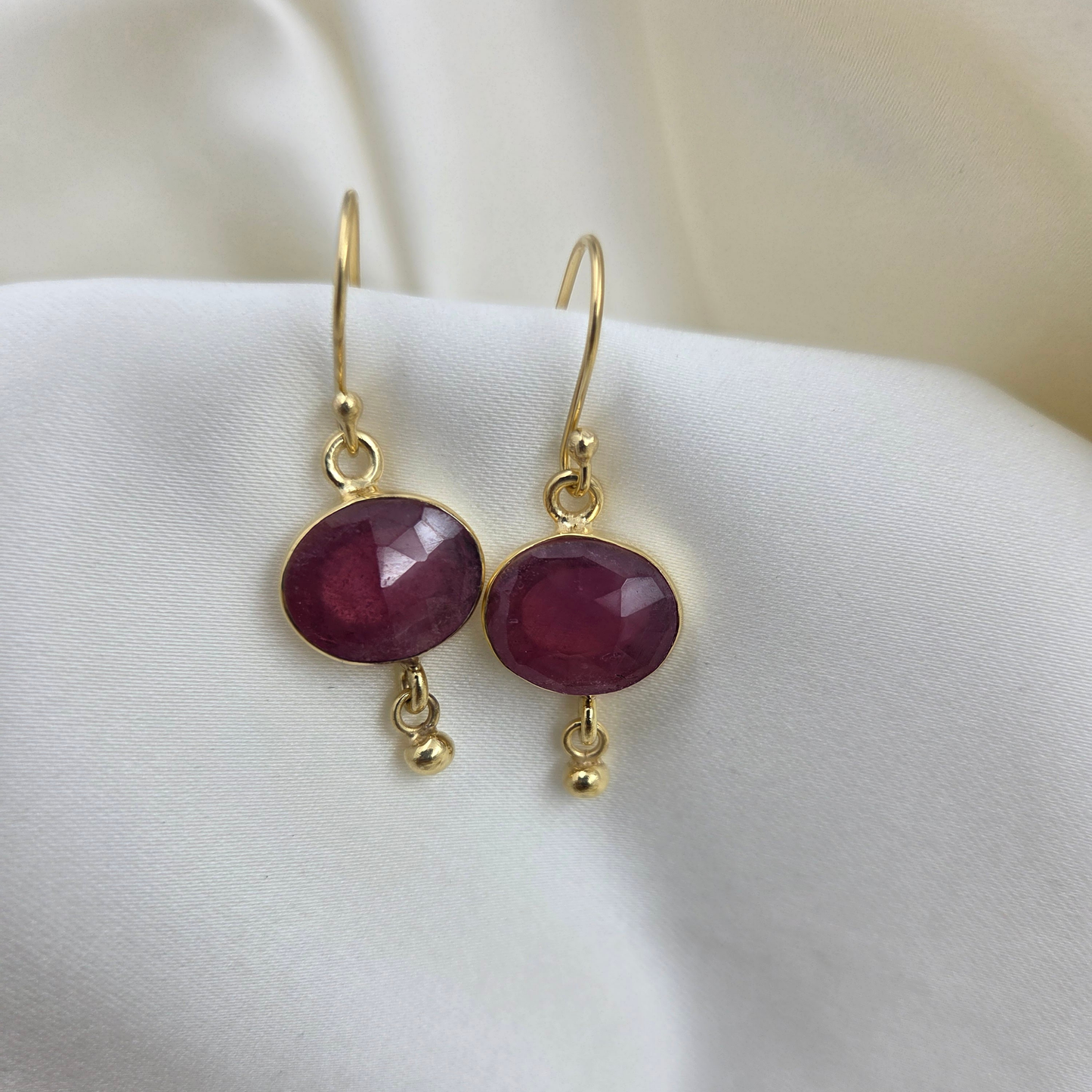 Silver earrings with ruby in 22 carat gold plating  - on a white surface