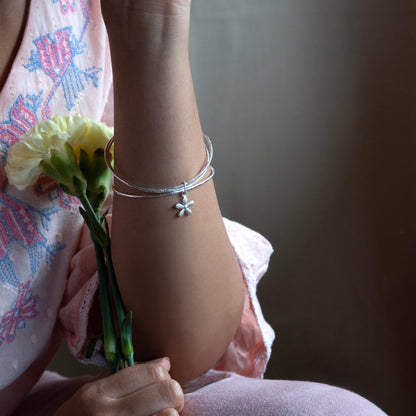 delicate silver bracelet with a small flower charm, styled with a pink patterned top and holding a yellow flower.