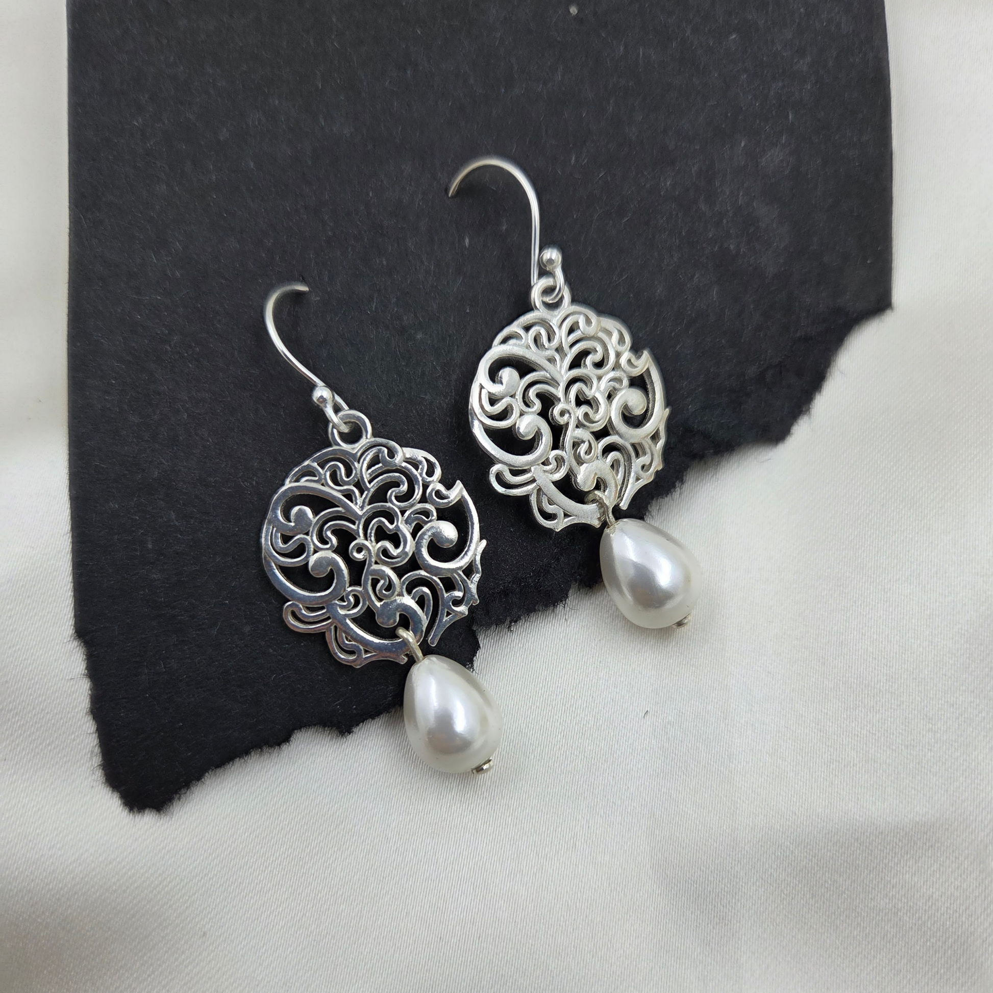 Silver filigree earrings with pearl drops on a black and white background
