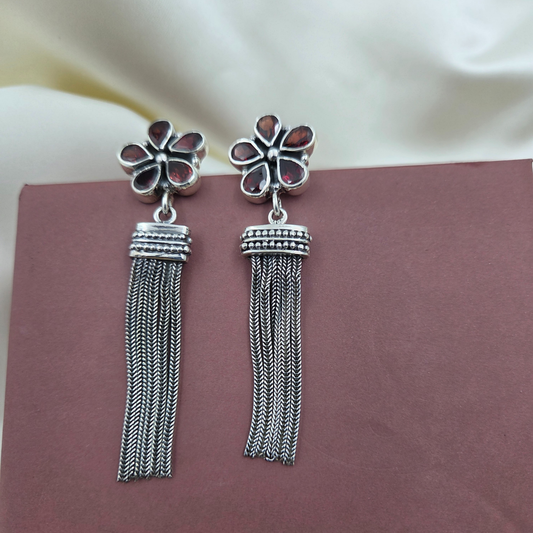 Silver tassel earrings with floral tops on a soft fabric background