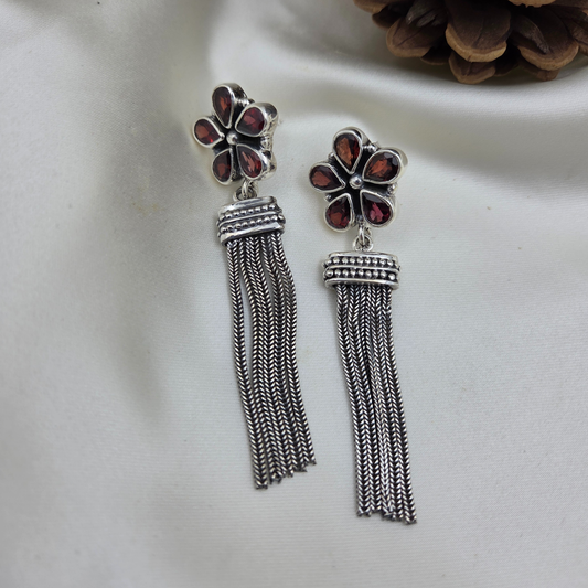 Silver tassel earrings with floral designs on a white surface.