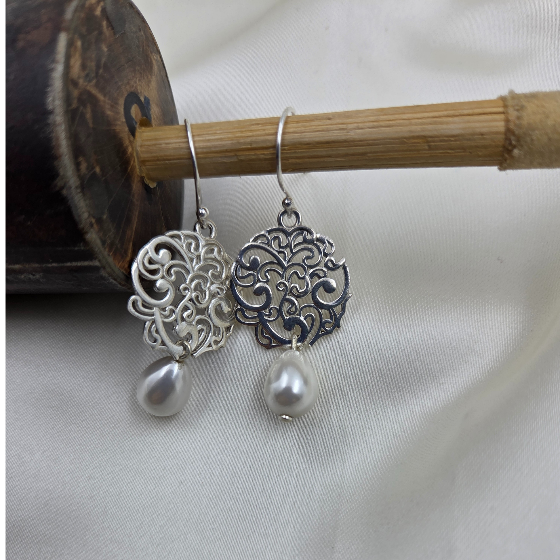 Silver earrings with intricate designs and pearl drops on a white background